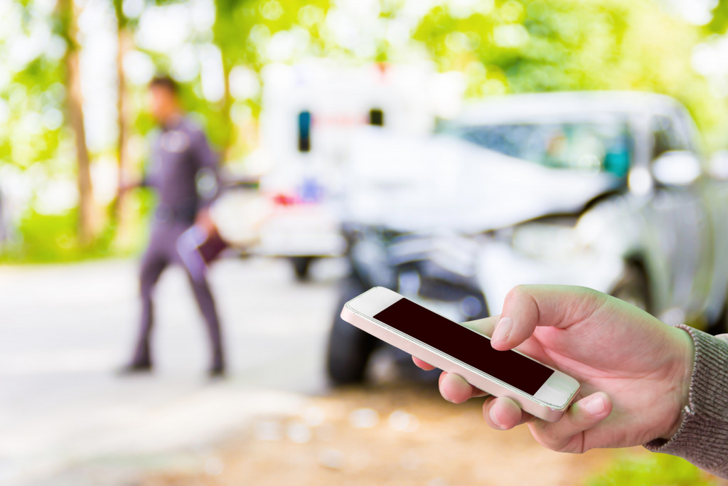 Person using their smartphone with a damaged vehicle in the foreground