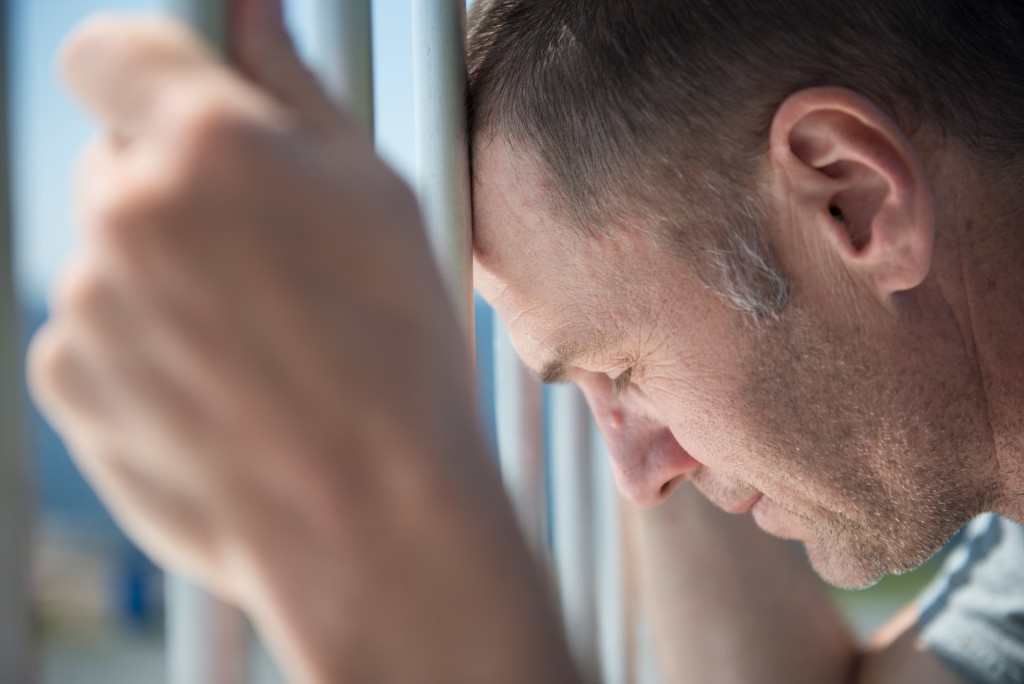 Depressed male inmate holds prison bars in despair