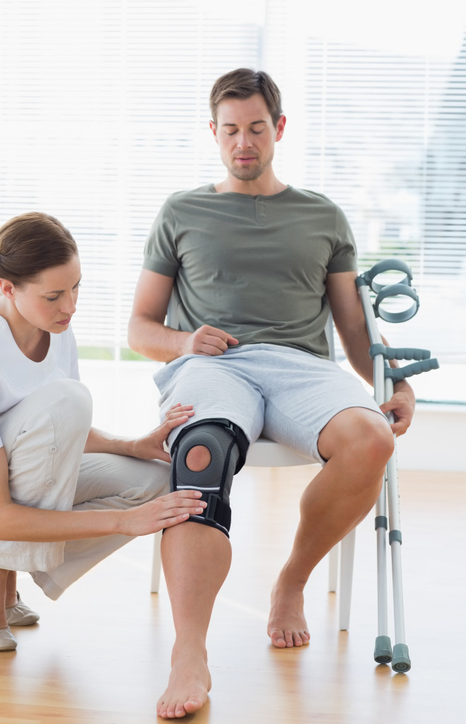 a man wearing knee support while a female therapist examines