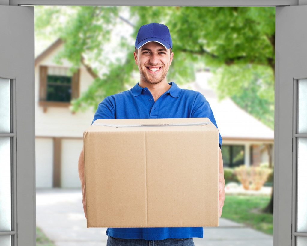 A smiling delivery man in uniform holding a big box on the front door
