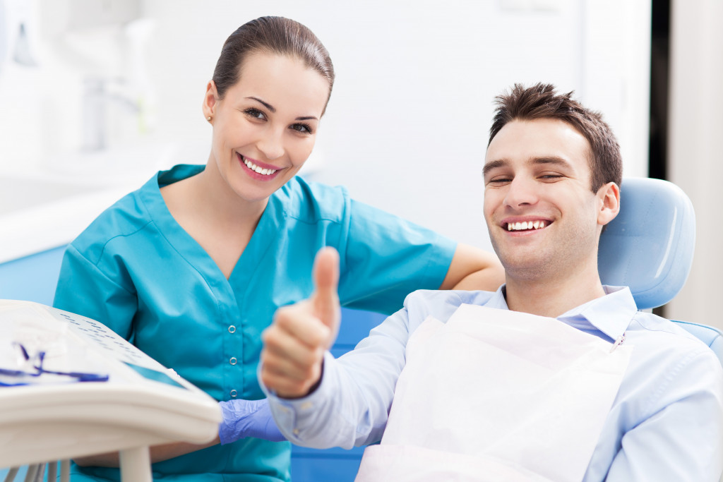 A male patient is pictured giving a thumbs up next to his female dentist.