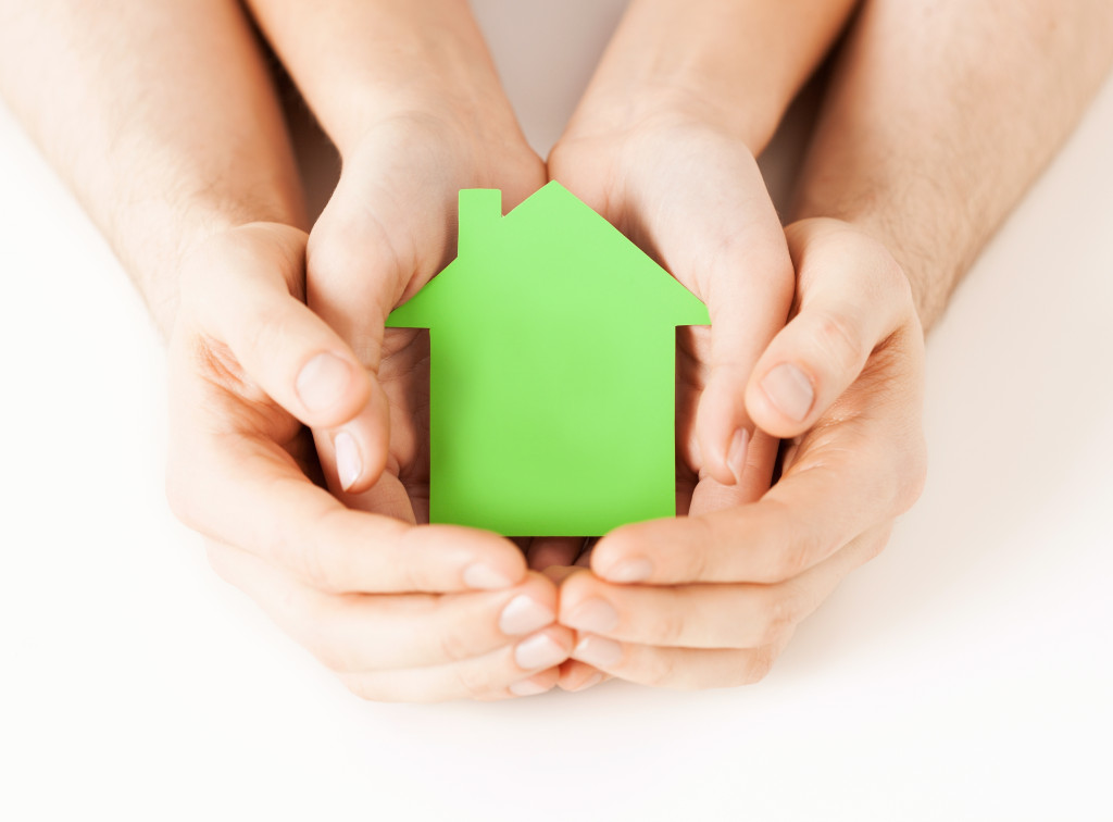 Closeup picture of male and female hands holding green blank paper house