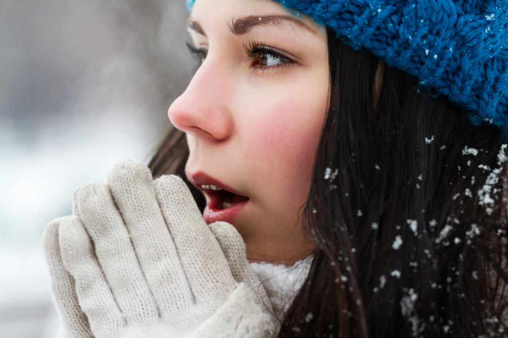 Young girl breathing warm air into her hands while staying outside during winter.