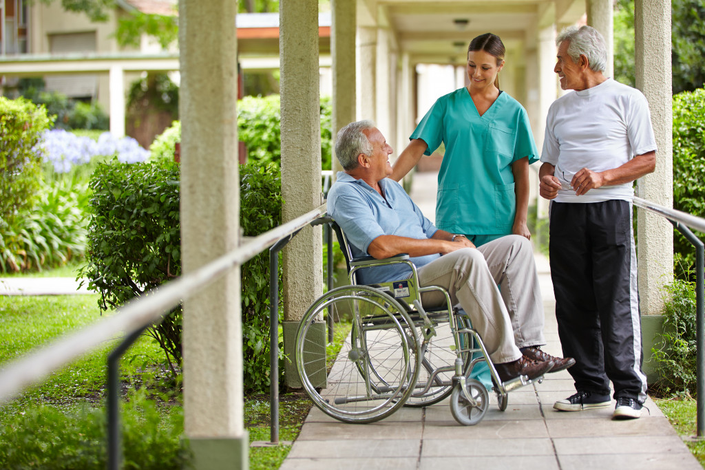 A nurse talking to two senior citizens at the garden of a hospital.