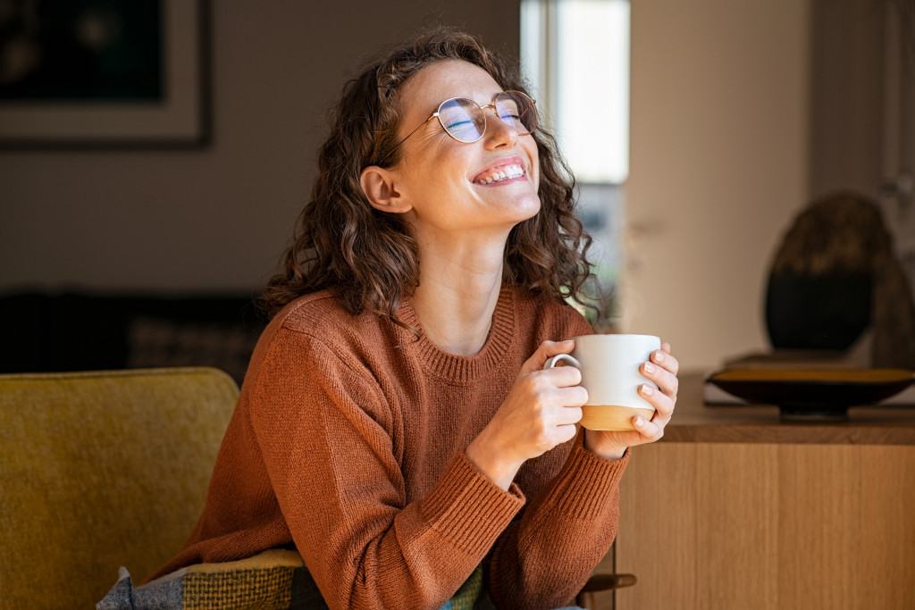 Smiling young woman sitting on a sofa at home while holding a cup of coffee.