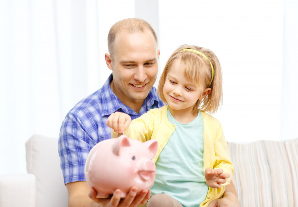 A little girl putting coin in a piggy bank, a father teaching about saving money