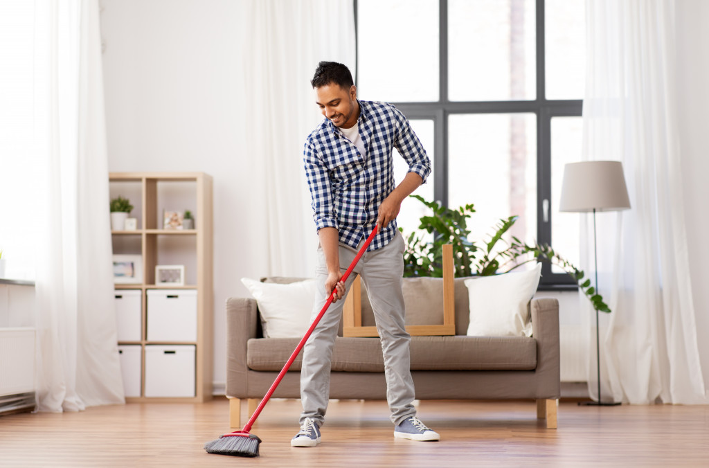 A man cleaning, sweeping the floor using an extended broom