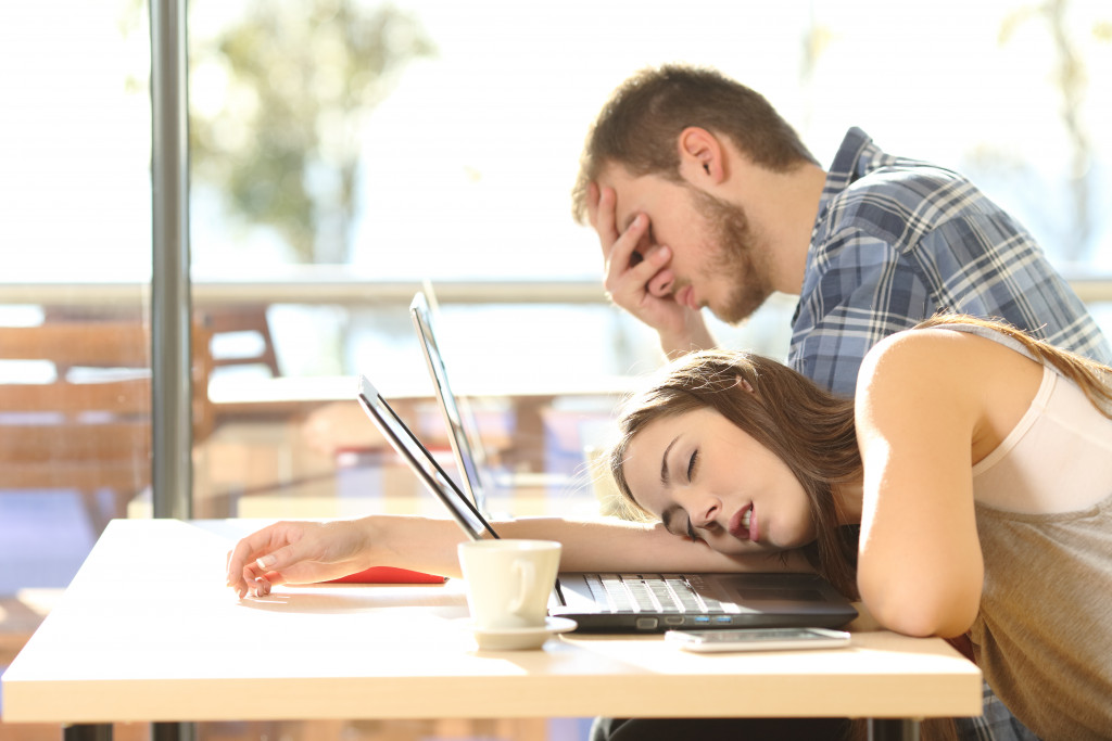 Two tired people trying to take a nap while working using their laptop in a cafe