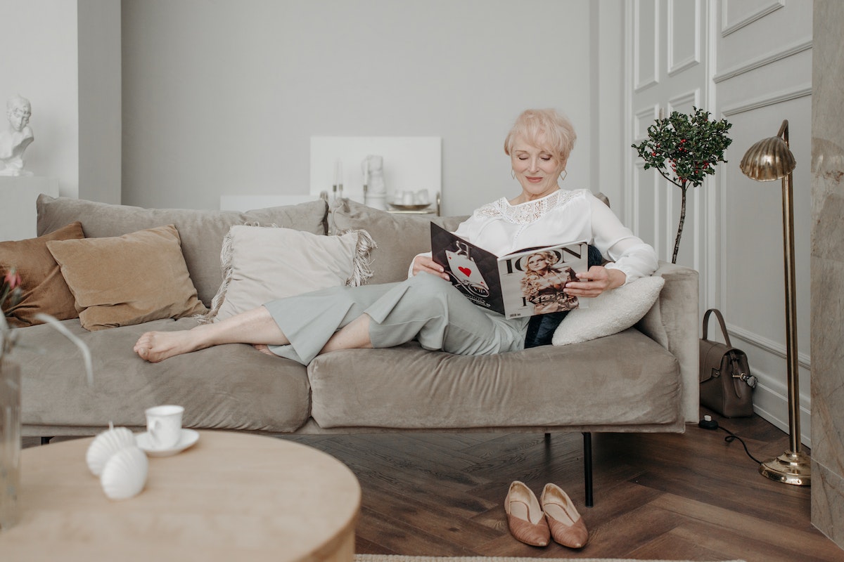 elderly woman reading a magazine on a sofa