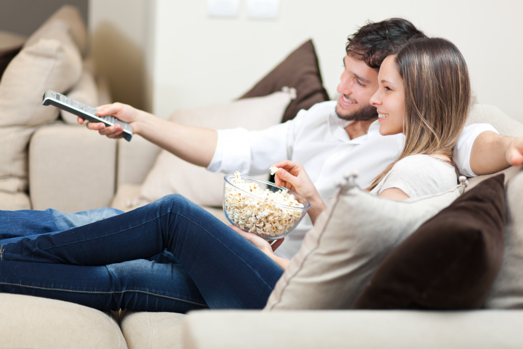 a couple sitting at a sofa with popcorn watching TV